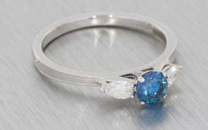 Three stone ring featuring a treated blue diamond, framed With stunning pear shaped diamonds